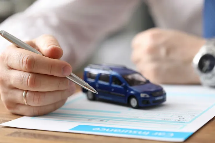 A close-up of a businessman holding a pen, signing a document next to a blue toy car on a desk